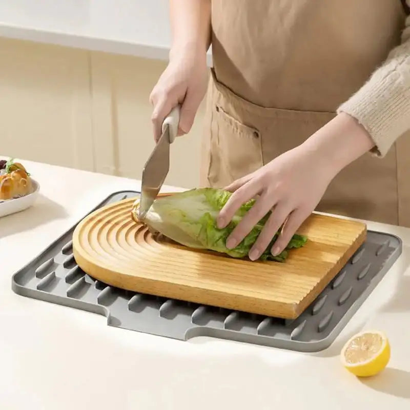 Person cutting lettuce on a wooden cutting board with a gray mat underneath