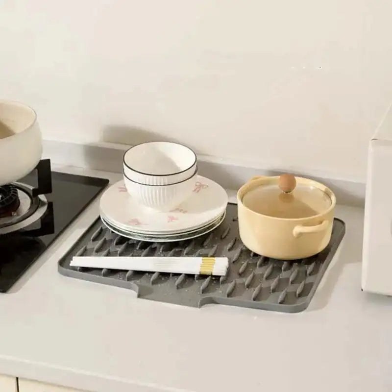 Gray silicone mat on a kitchen counter with dishes and a pen on top