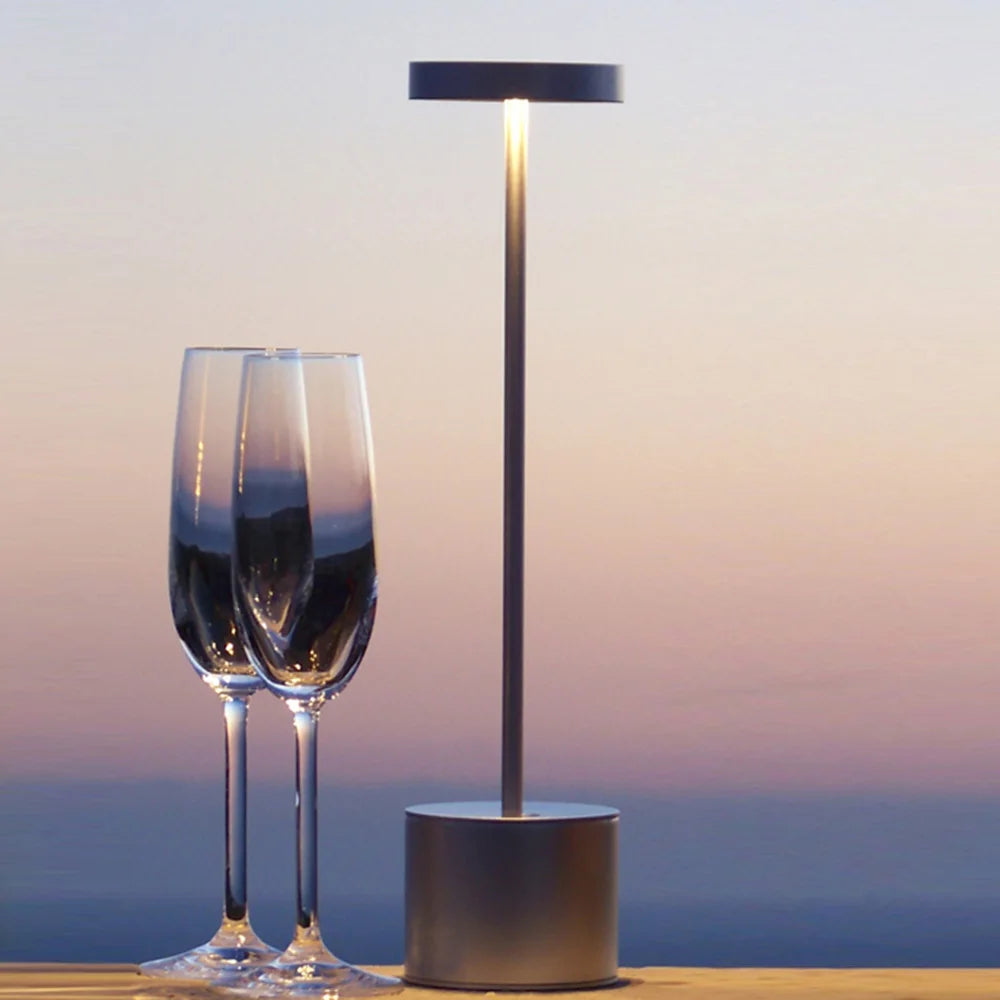 Table lamp with two wine glasses on a surface with a sunset or sunrise background.