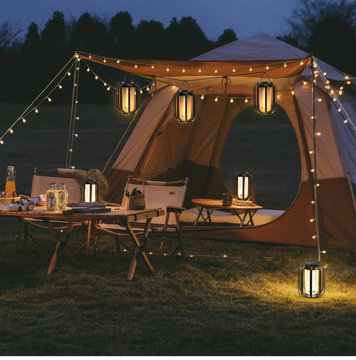 Camping setup with a tent, lanterns, and string lights in a field at night.