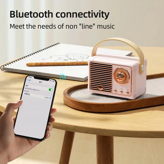 Hand connecting smartphone to retro pink Bluetooth speaker with gold accents on a table, showcasing wireless audio pairing