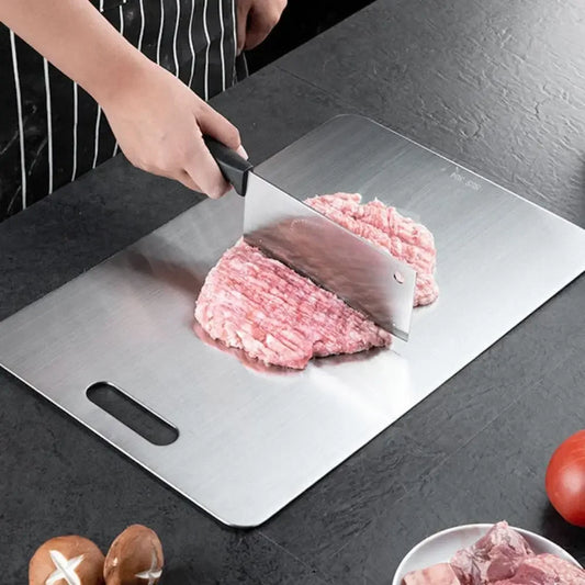 Person using a stainless steel cutting board to chop raw meat with a cleaver on a black kitchen countertop