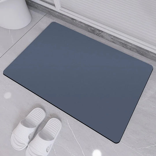 Gray bath mat on a bathroom floor with white slippers nearby