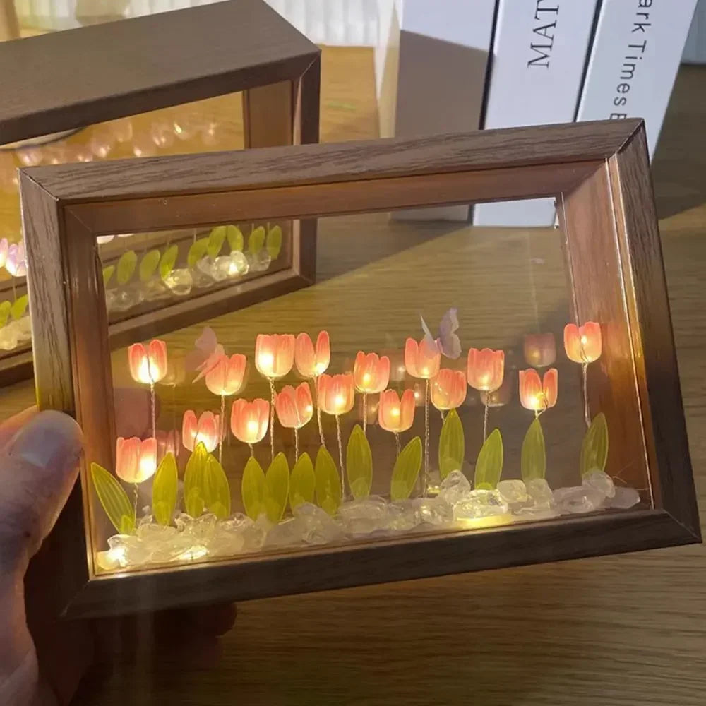 Hand holding a DIY wooden tulip light box with glowing pink LED flowers, green leaves, and butterfly accents on a crystal bed